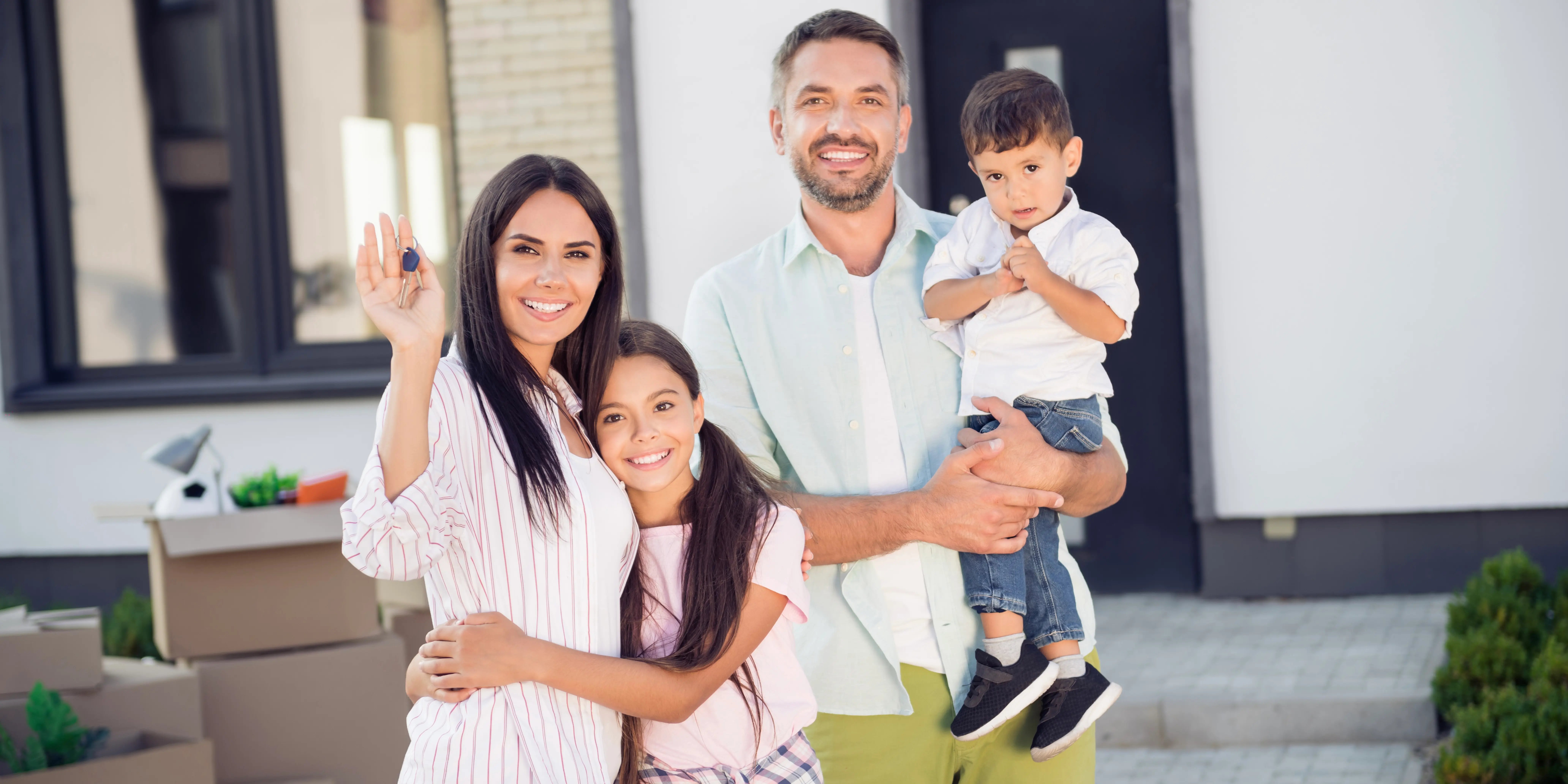 Familia afuera de la casa nueva que acaban de comprar, hay cajas de mudanza