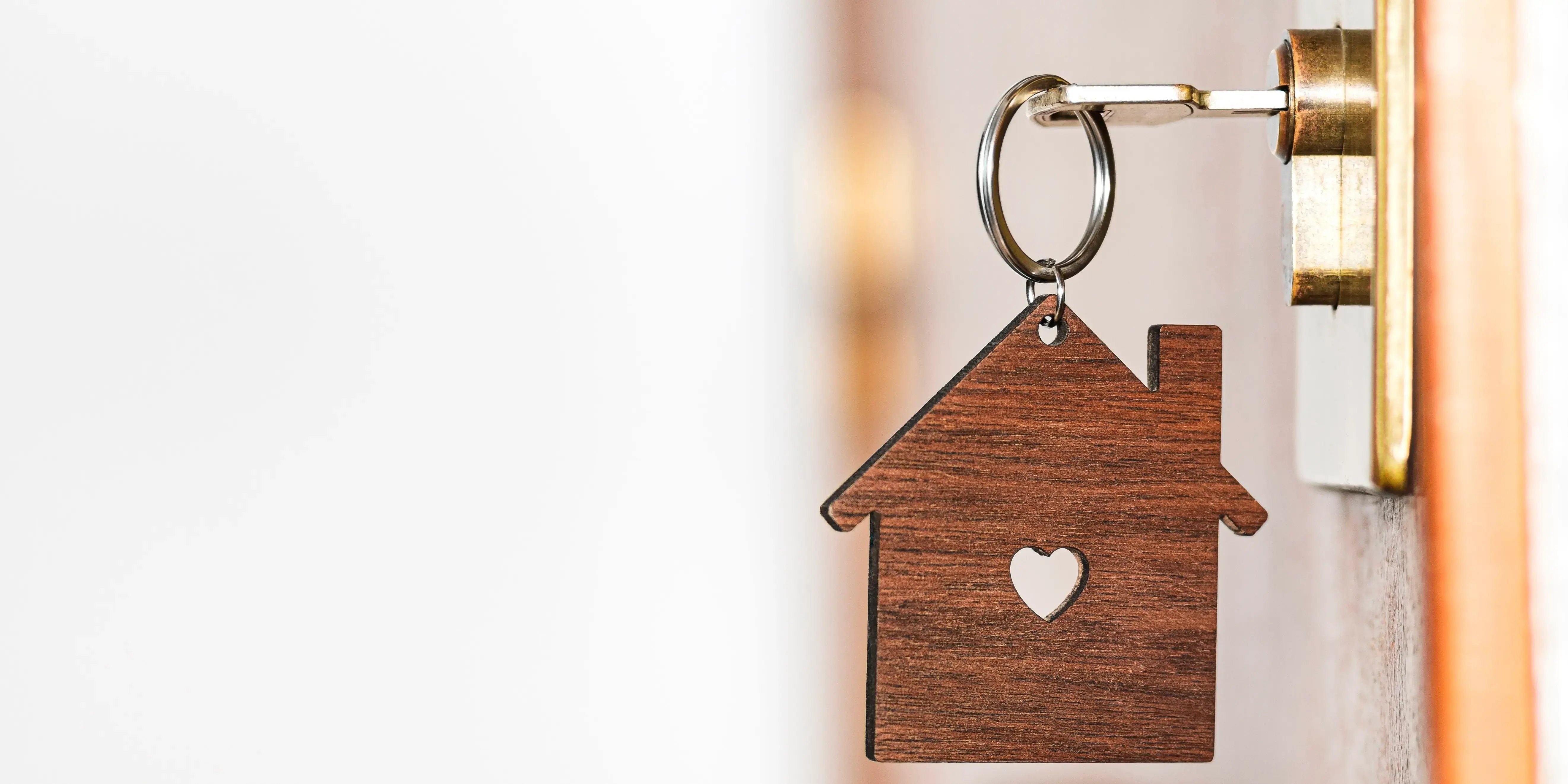 Llavero de madera en forma de casa insertado en la cerradura de una puerta delantera de una casa